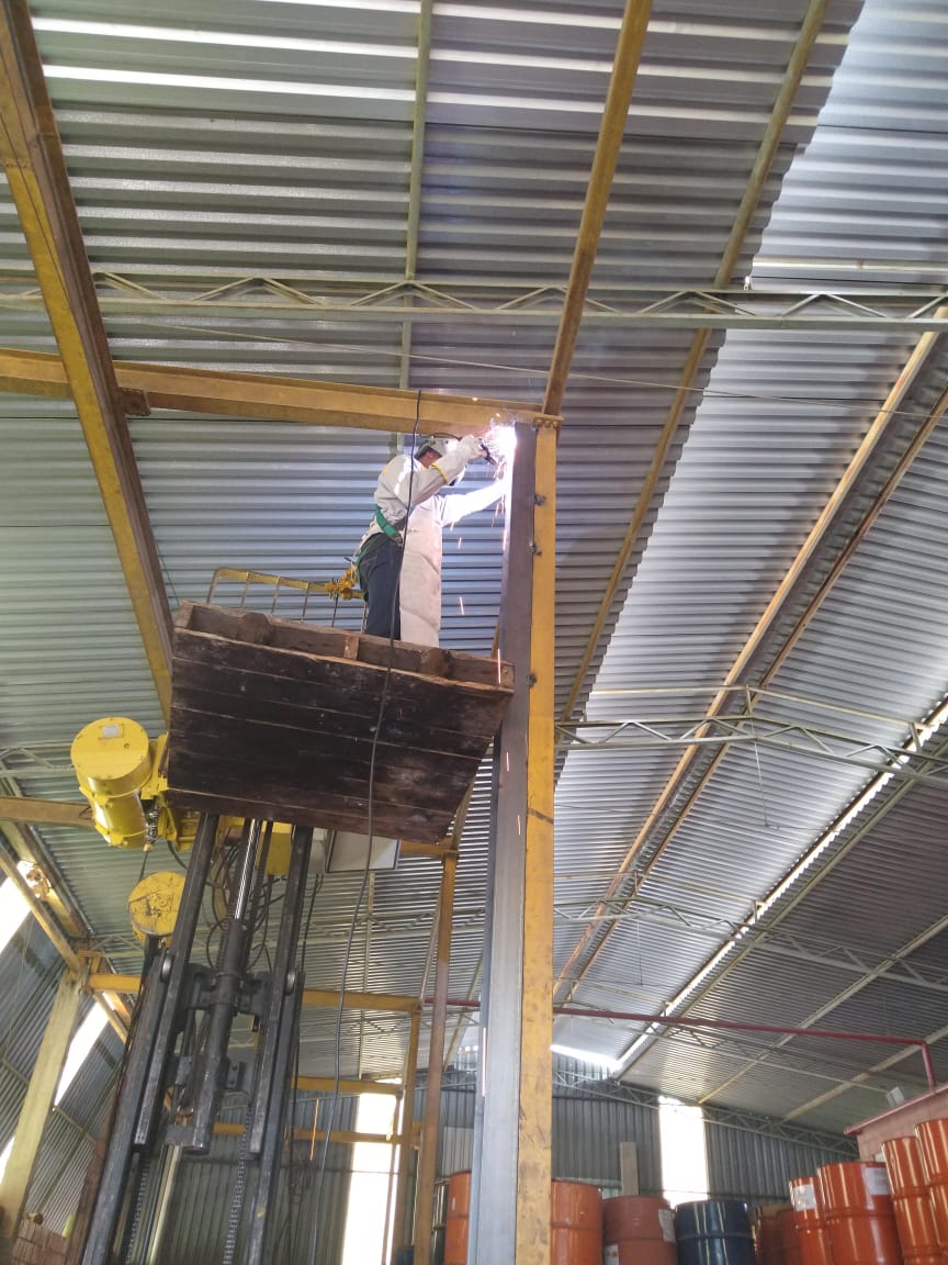 Soldador em plataforma elevada realizando reforço de estrutura metálica